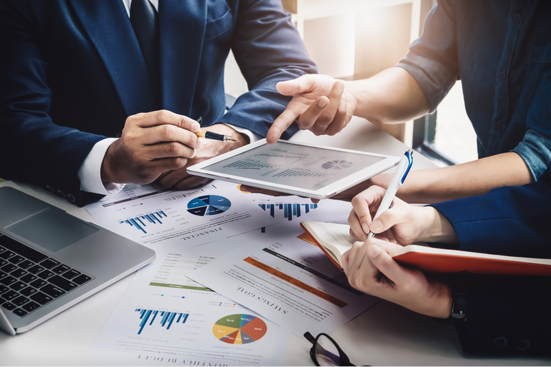 Three people discuss financial charts and graphs during a business meeting.