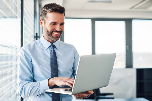 A businessman smiles while working on a laptop in a modern office, highlighting Dubai's business-friendly environment.